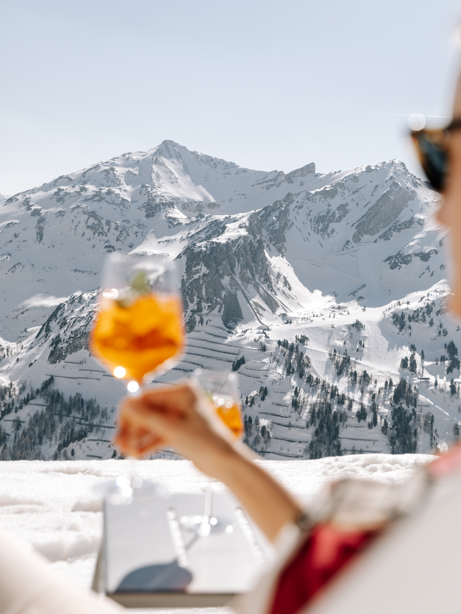 Person mit Aperol Spritz Getränk mit Bergpanorama im Hintergrund